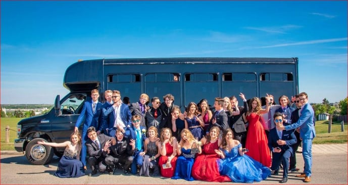 Group of high school grads dressed up in front of black party bus